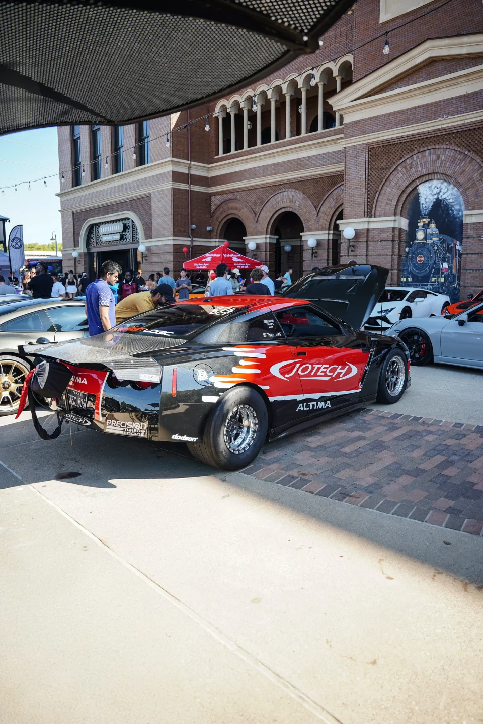 A black and red Jotech Nissan GT-R R35 drag car with a widebody kit and parachute parked at an outdoor car show.