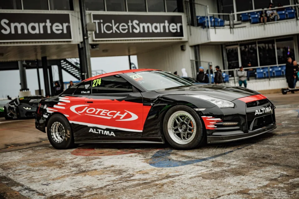 A black and red Jotech Nissan GT-R race car with drag slicks at a drag strip staging lane.