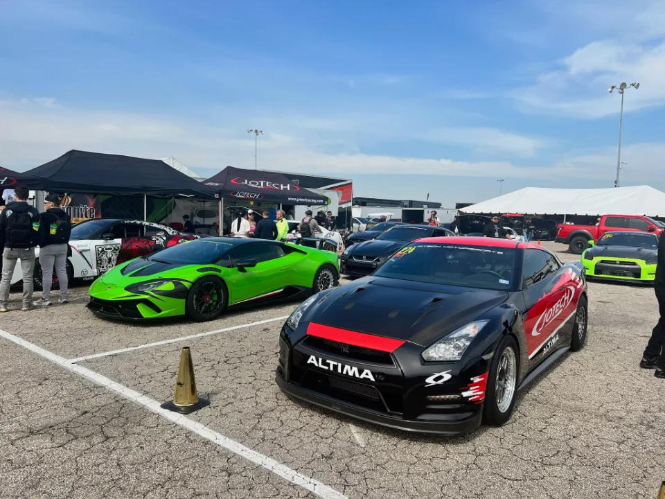Modified Nissan GT-R and green Lamborghini Huracan parked at a Jotech Motorsports event with tents and spectators.