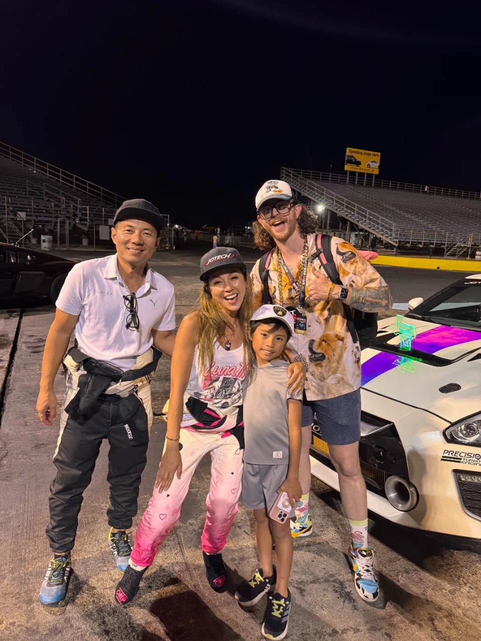 Group photo of Jotech team members and a child posing in front of a white Nissan GT-R at a drag strip at night.