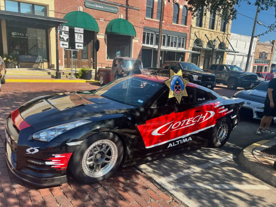 Black and red Jotech Nissan GT-R drag car with custom livery parked on a brick street at an outdoor car show.