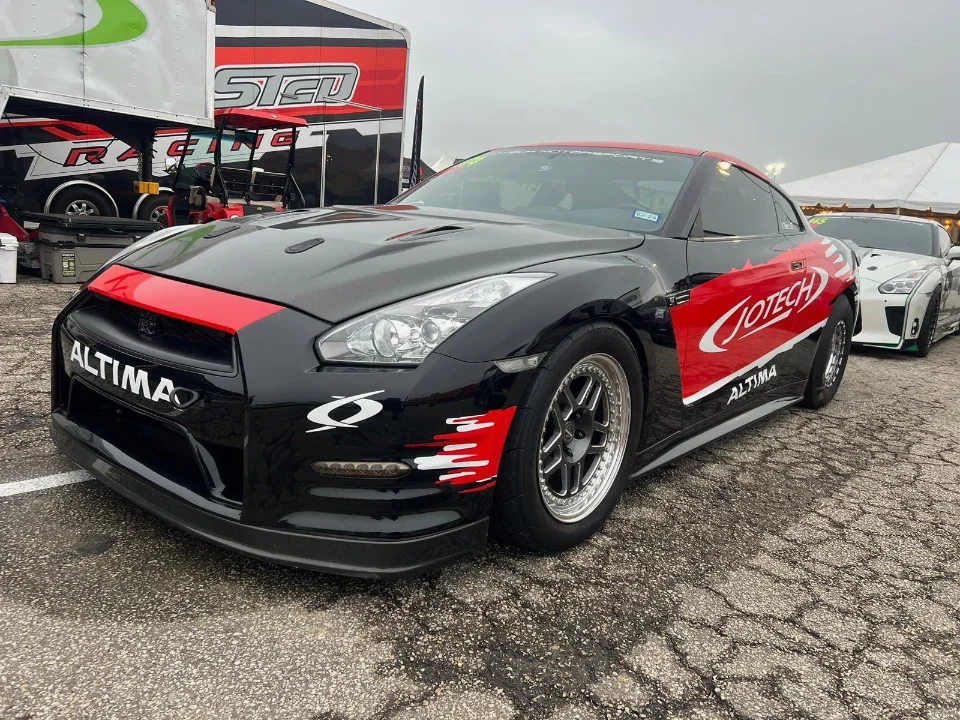 A black and red Nissan GT-R drag car with Jotech Motorsports livery parked at a track event next to a racing trailer.