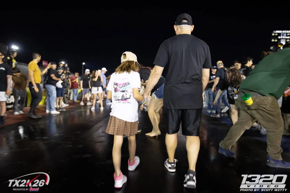 Spectators walk on the drag strip at night during the TX2K26 event, captured by 1320 Video.