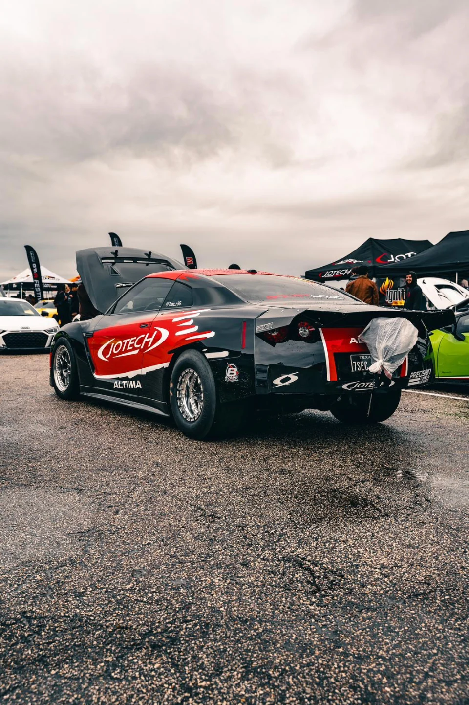 A black and red Jotech Nissan GT-R drag car with its hood open at a track event, featuring large rear slicks.