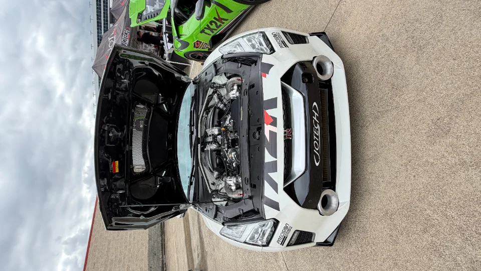A white Nissan GT-R with its hood open, showcasing a highly modified twin-turbo engine by Jotech Motorsports.