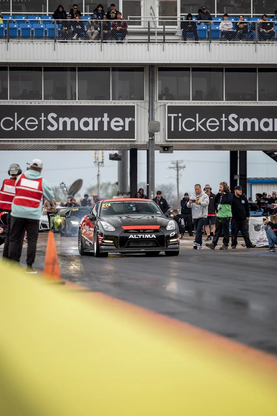 A black Nissan GT-R with Jotech Motorsports livery on a drag strip, preparing to race. Spectators are visible in the stands.