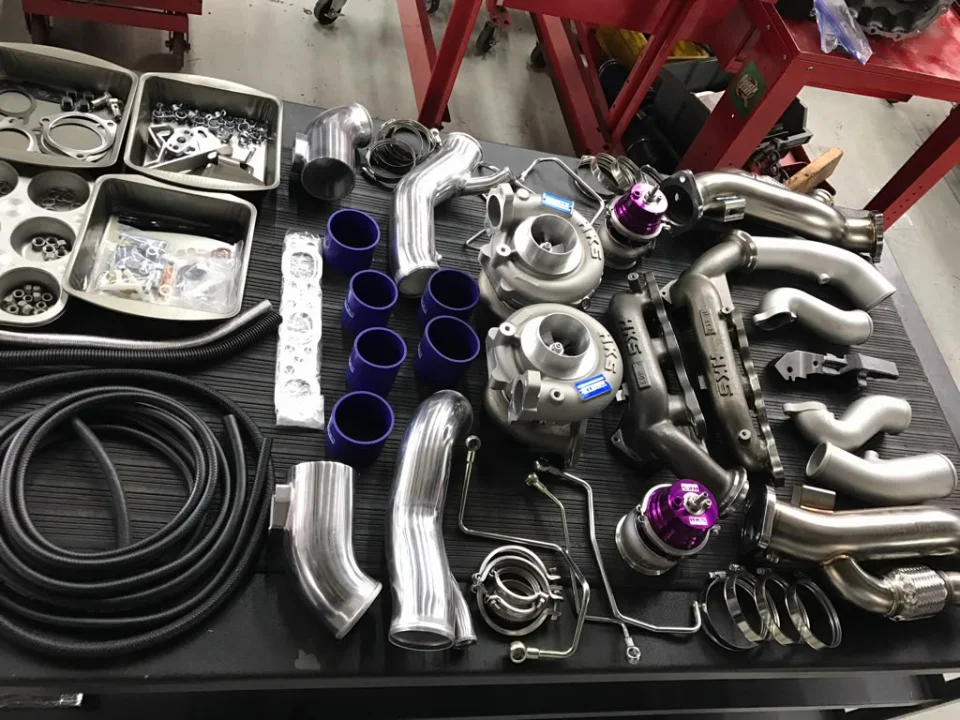 A collection of HKS turbochargers, wastegates, exhaust manifolds, and boost piping laid out on a workbench.