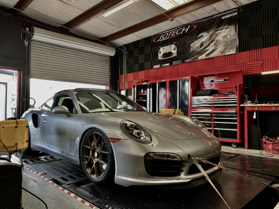 A silver Porsche 911 strapped to a dynamometer at Jotech Motorsports, ready for performance tuning.