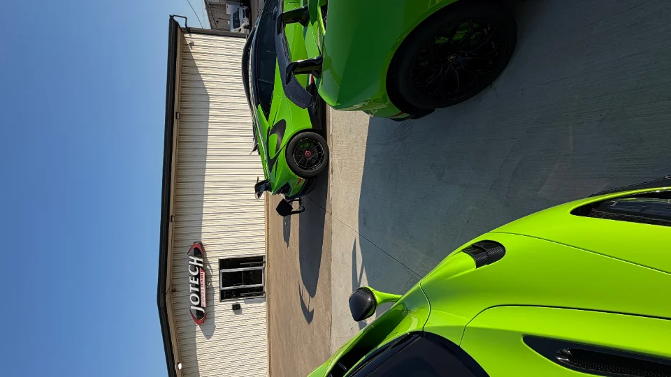Two vibrant green McLarens parked outside the Jotech Motorsports performance tuning shop on a sunny day.
