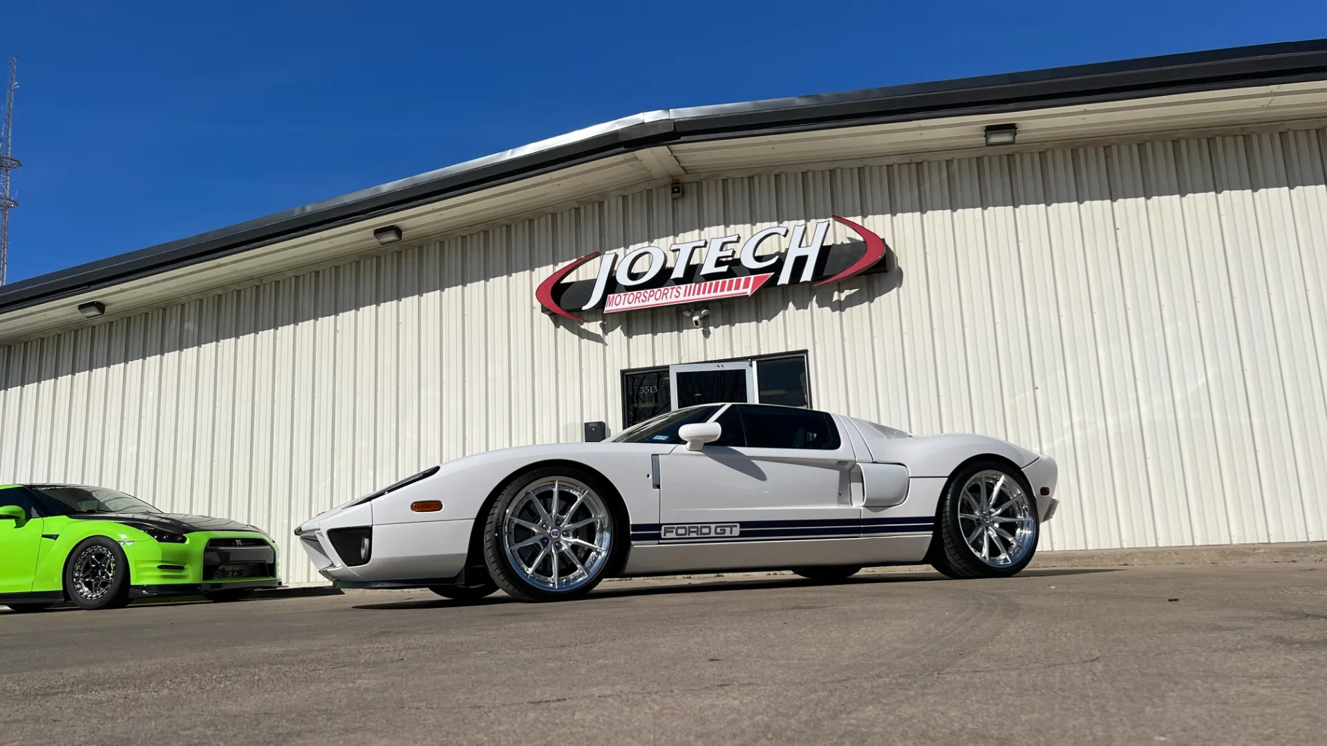 A white Ford GT and a green Nissan GT-R parked outside the Jotech Motorsports shop building.