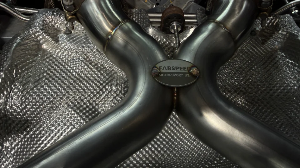 Close-up of a Fabspeed stainless steel exhaust system with heat shielding on a performance car.