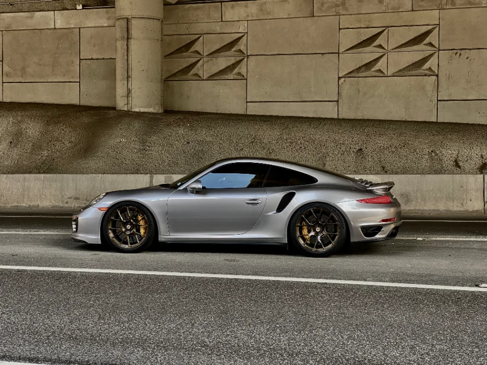 Silver Porsche 911 with custom bronze wheels parked under a concrete overpass, showcasing its sleek profile.