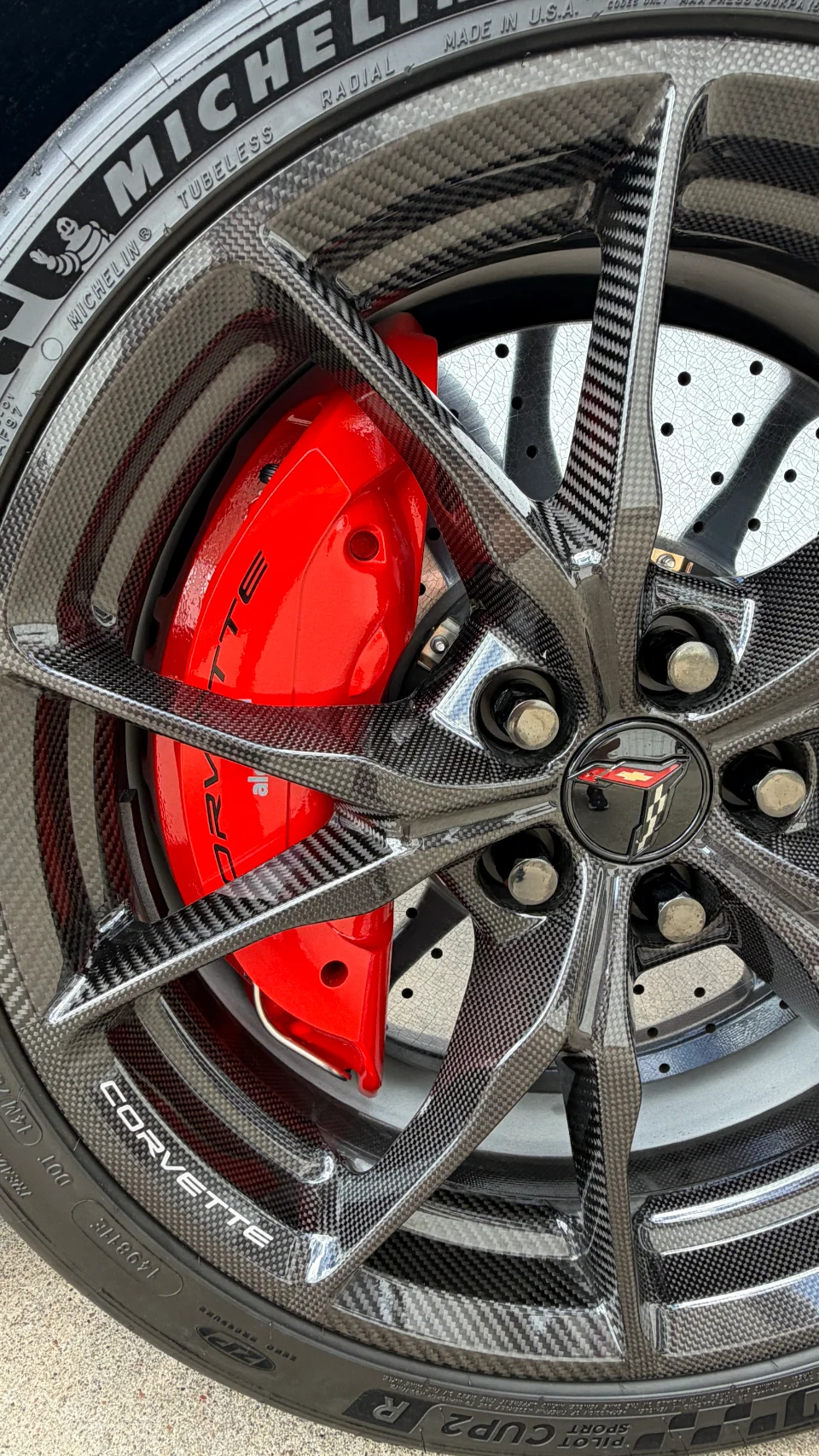 A close-up detail of a Corvette's carbon fiber wheel, red brake caliper, and Michelin tire.