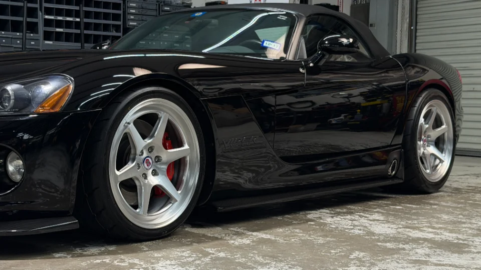 A sleek black Dodge Viper convertible with custom silver multi-spoke wheels and red brake calipers parked indoors.