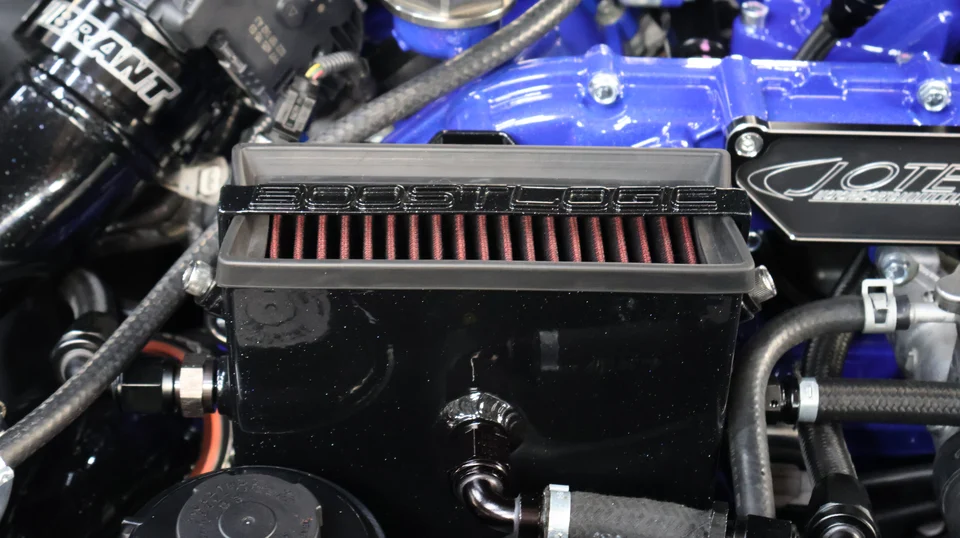 Close-up of a custom engine bay featuring a BoostLogic air filter and blue intake manifold.