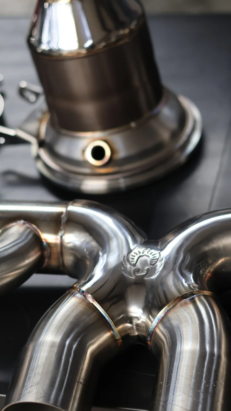 Close-up of polished stainless steel exhaust components with visible welds and a Jotech Motorsports logo.