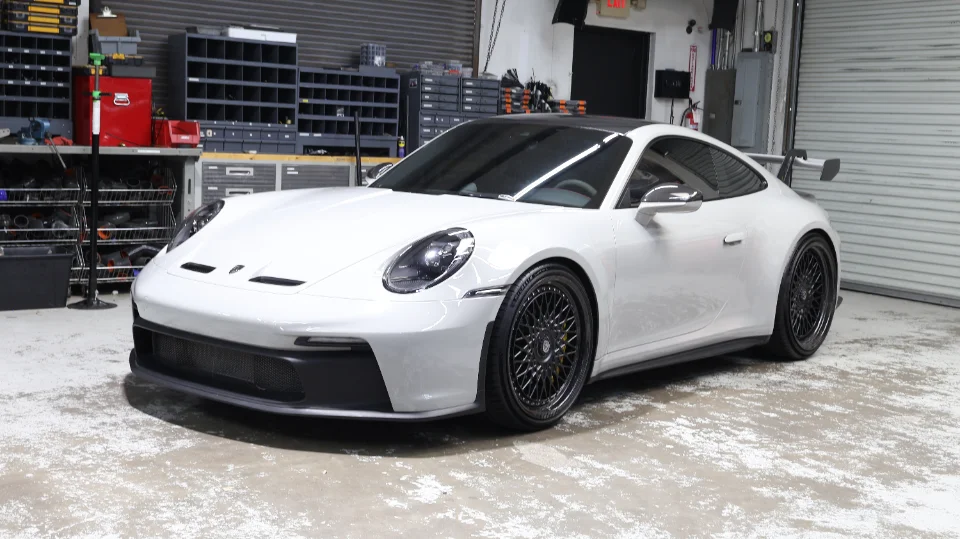 A pristine white Porsche 911 GT3 with custom black multi-spoke wheels parked inside a performance tuning shop.