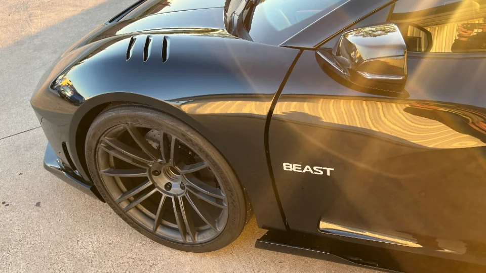 Close-up of a black car's front wheel, fender with vents, and side panel featuring the 'BEAST' logo.