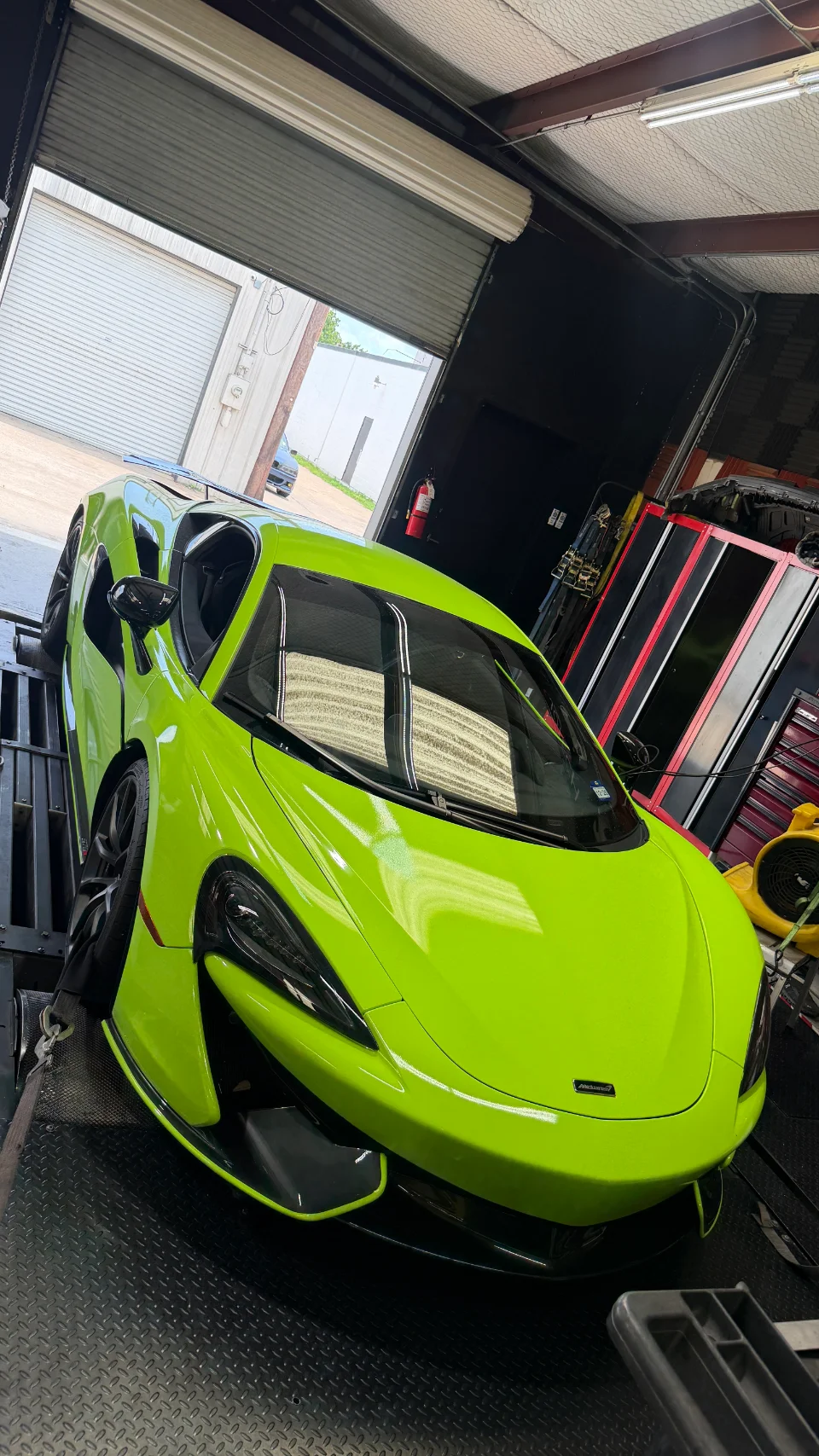 A vibrant lime green McLaren supercar is strapped down on a dynamometer inside a performance tuning shop, ready for testing.