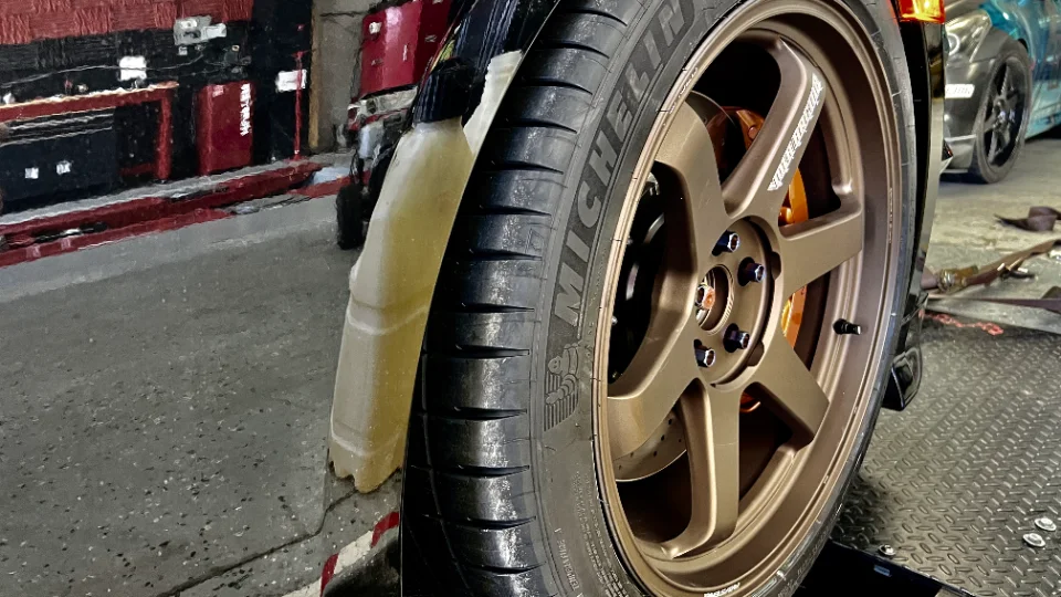Close-up of a car's bronze Volk TE37 wheel with Michelin performance tires, likely in a shop or dyno setting.