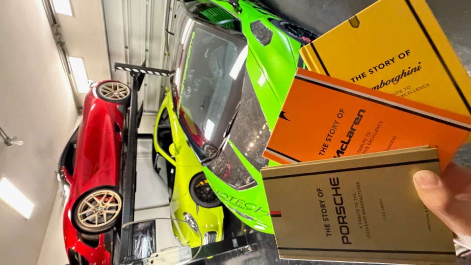 A Jotech garage with a red sports car on a lift and a green Lamborghini, with books about Lamborghini, McLaren, and Porsche.