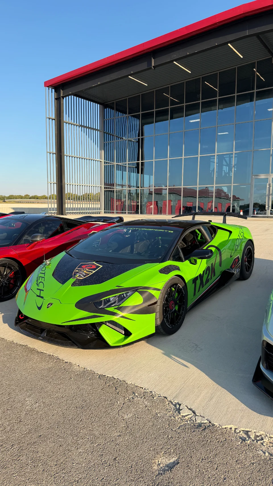 A bright green Lamborghini Huracan with custom Jotech livery and carbon fiber aero parked outside a modern building.