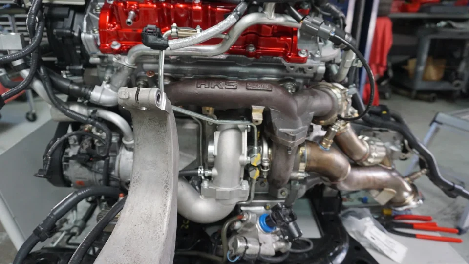 Close-up of a high-performance engine featuring an HKS turbocharger system, likely undergoing assembly or modification in a shop.