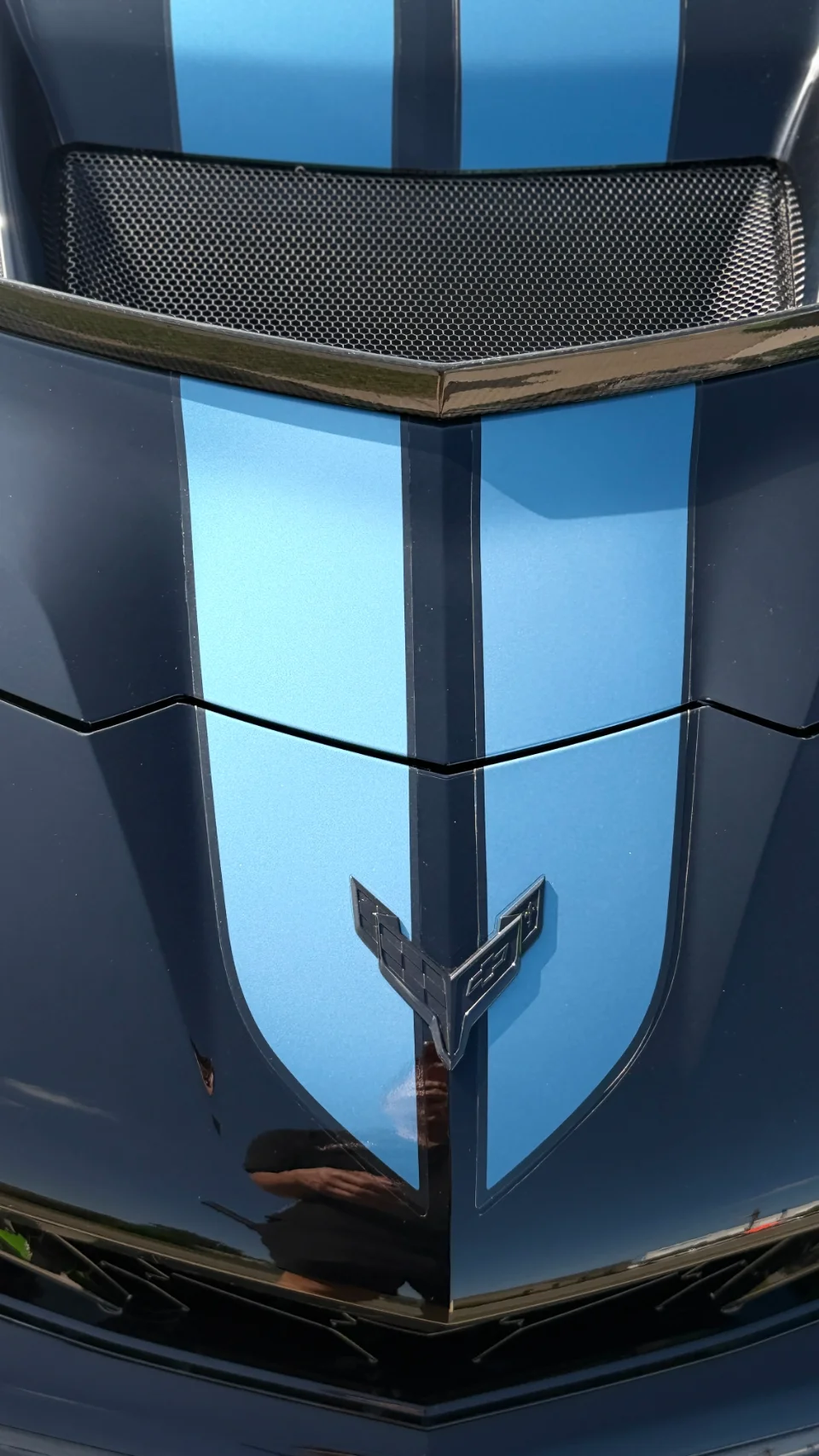 Close-up of a black Chevrolet Corvette hood with blue racing stripes and the Corvette emblem.