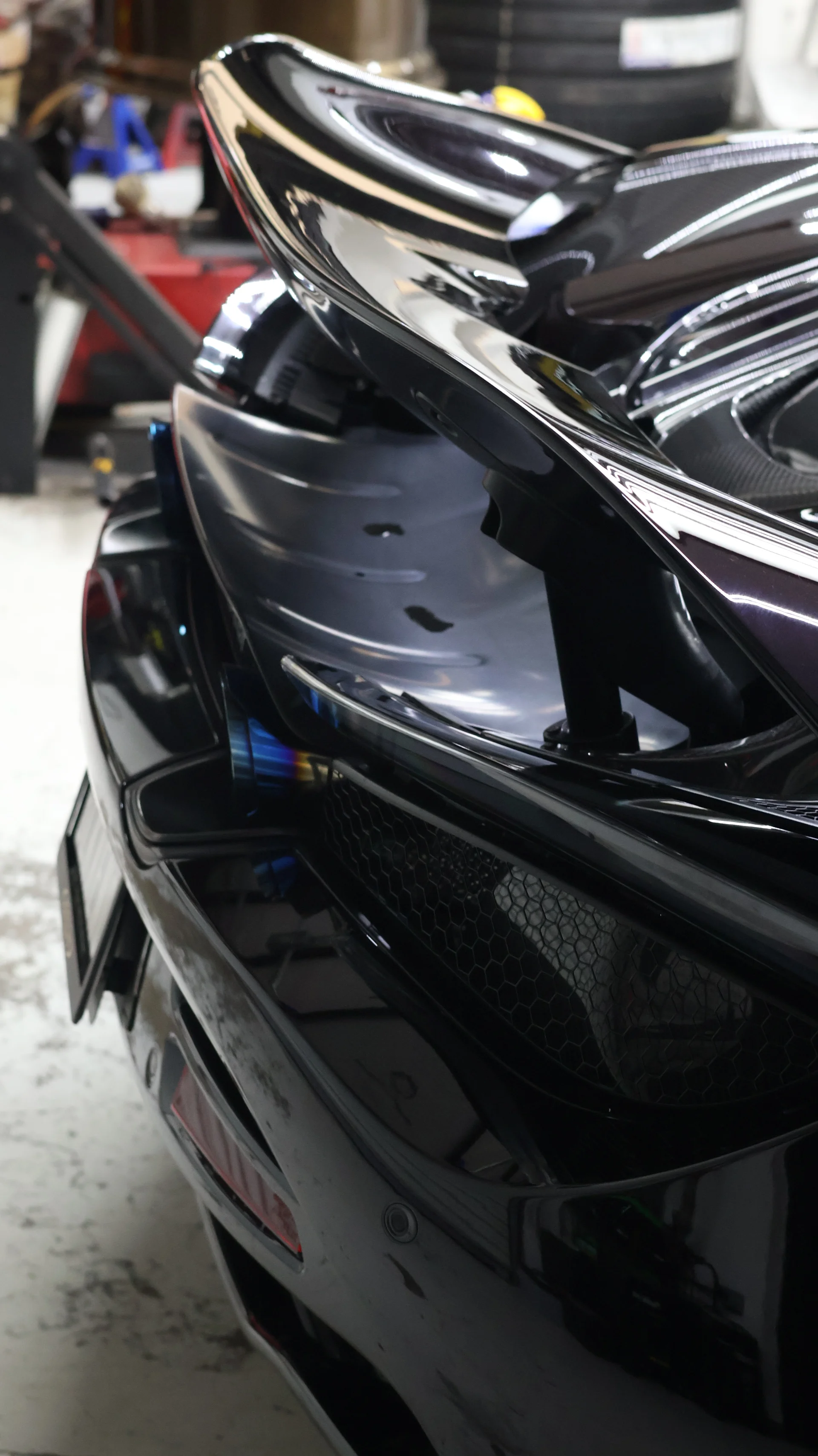 Close-up of the rear of a black McLaren supercar, highlighting its active aerodynamic wing and burnt titanium exhaust tip.