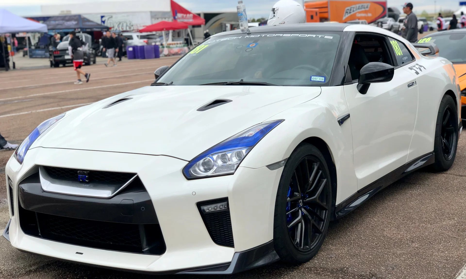 A white Nissan GT-R with blue headlight accents and black wheels parked at a track event.