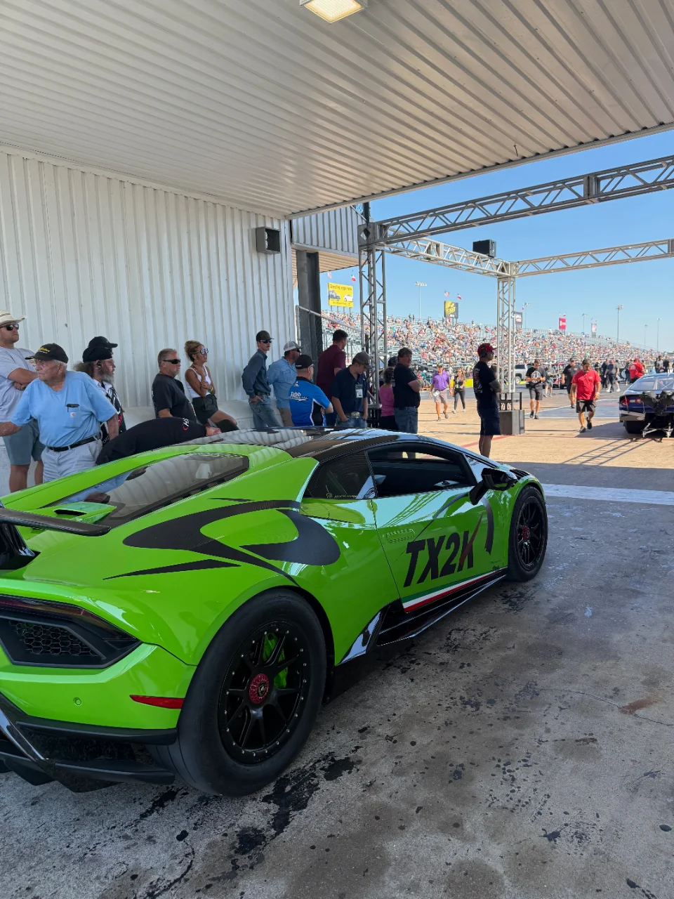 A bright green Lamborghini Huracan with TX2K livery in the staging lanes at a drag racing event, with spectators in the background.