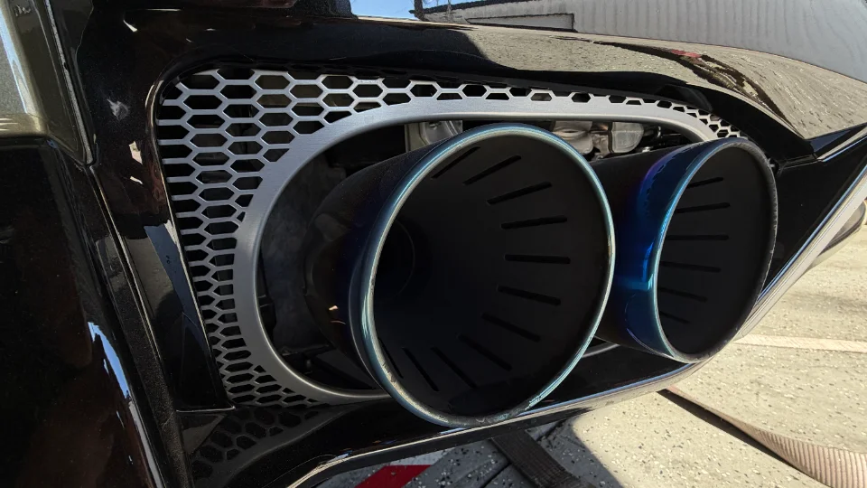 A close-up of a car's rear bumper featuring large, blue-tinted aftermarket exhaust tips and a honeycomb grille.