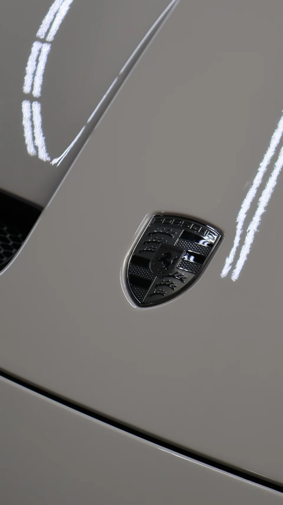Close-up detail shot of a chrome Porsche emblem on the white body of a luxury sports car.
