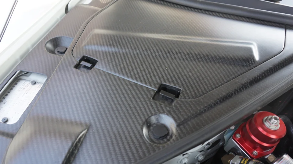 Close-up of a car's engine bay featuring carbon fiber covers and a red aftermarket fuel pressure regulator.