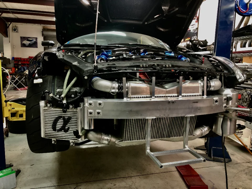Front view of a Nissan GT-R in a shop with its bumper removed, showcasing large intercoolers, boost piping, and an Alpha oil cooler.
