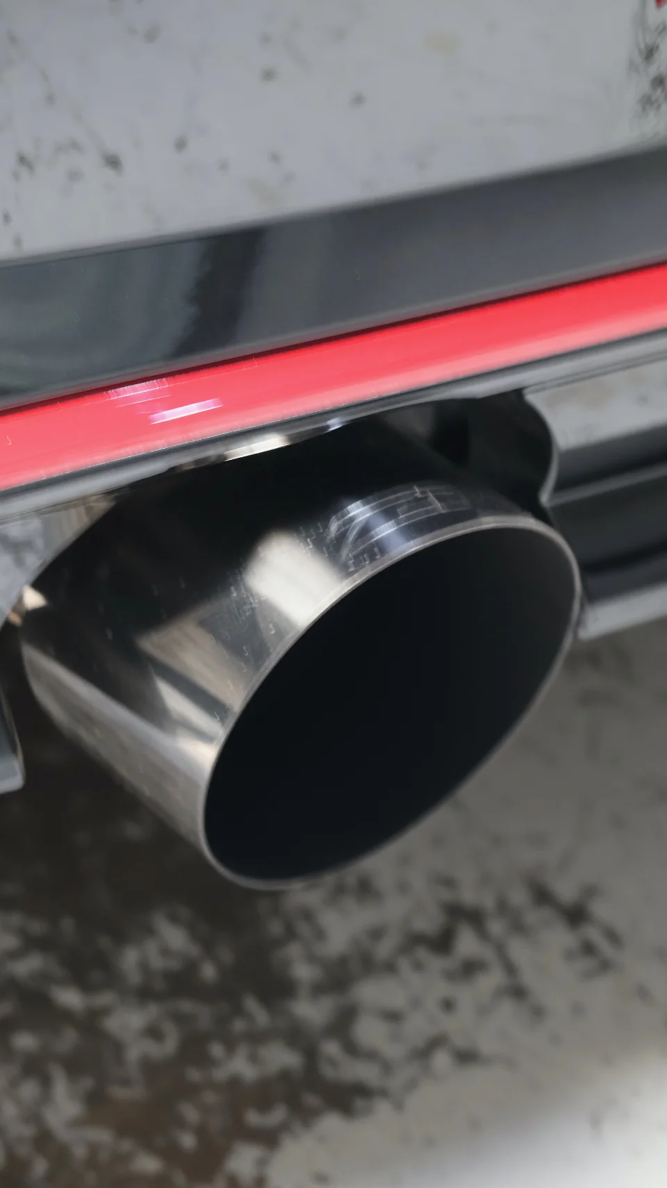 Close-up of a polished aftermarket exhaust tip on a car with a red accent line on the rear bumper.