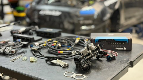 Various performance electronics, wiring harnesses, and sensors laid out on a table in a Jotech Motorsports shop.