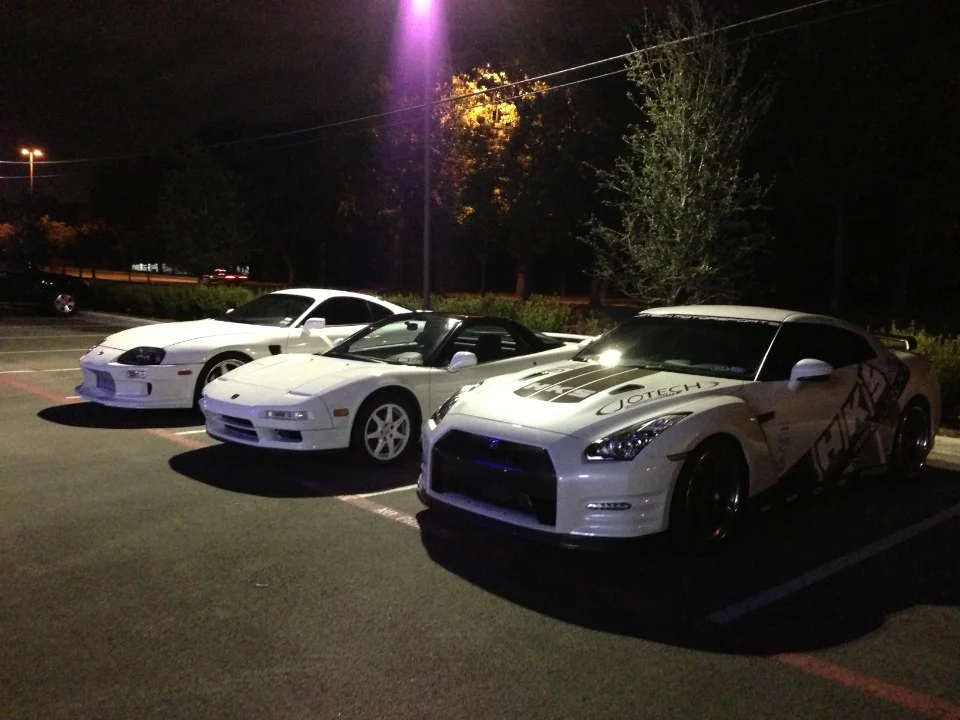 Three white sports cars, a Toyota Supra, Honda NSX, and Nissan GT-R, parked together at night.
