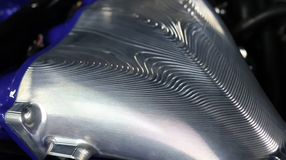 Close-up of a custom machined aluminum intercooler with intricate fin patterns in an engine bay.