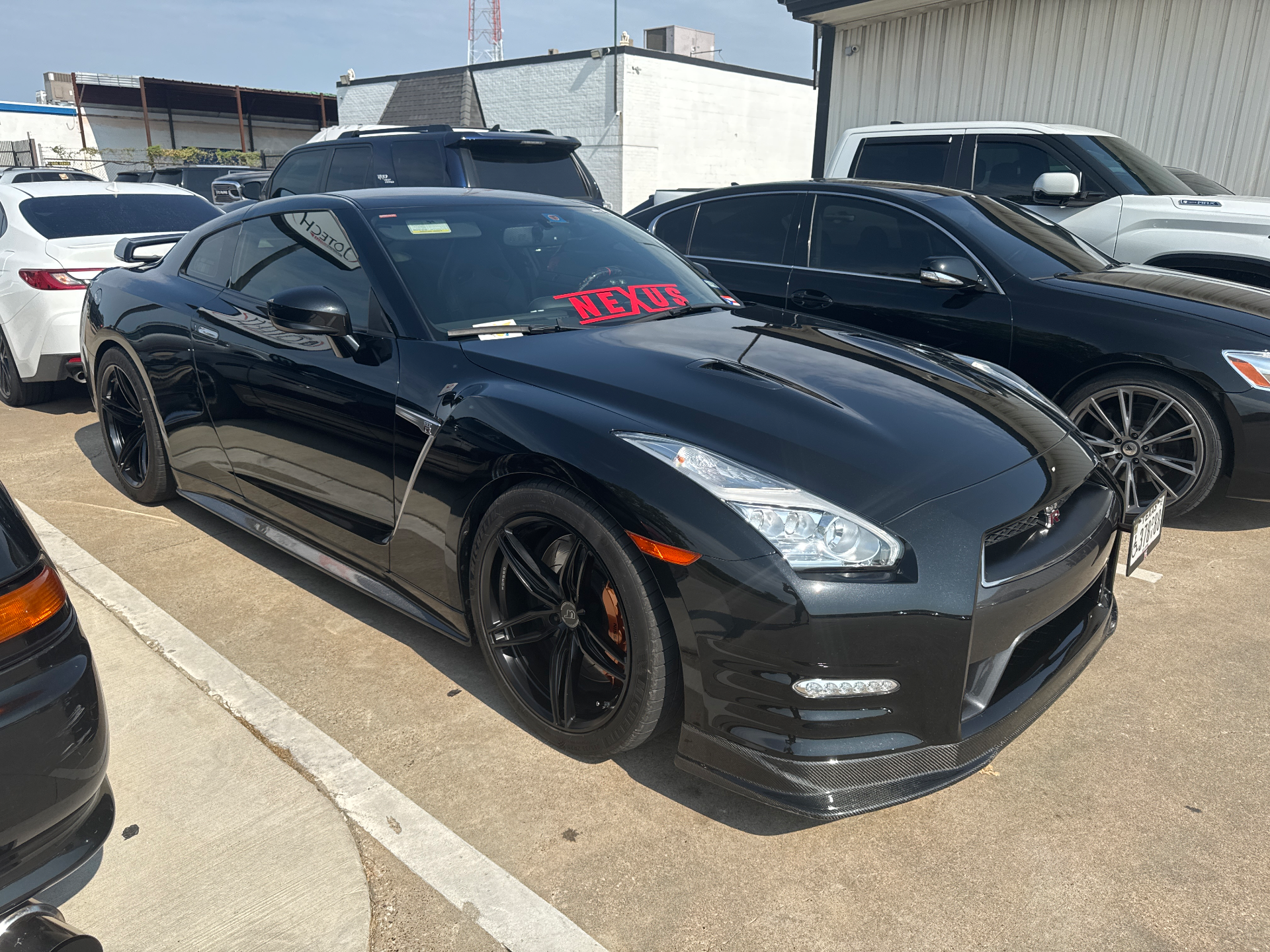A black Nissan GT-R with carbon fiber aero and aftermarket wheels parked outdoors.