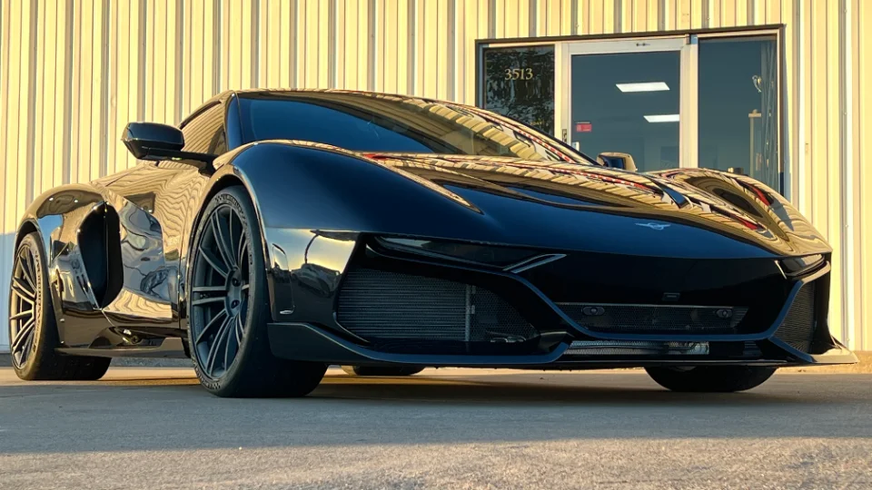 A sleek black custom sports car parked in front of a building, showcasing its aggressive front design and glossy finish.
