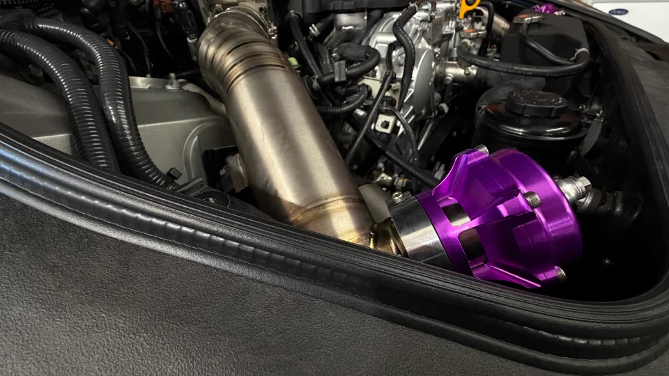 A close-up of a car's engine bay showing a purple blow-off valve and custom turbo piping.