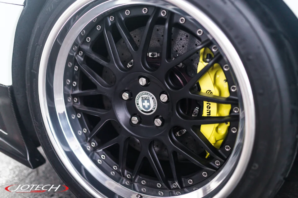 Close-up of a car's black HRE performance wheel with a polished lip, yellow Brembo brake calipers, and perforated rotors.