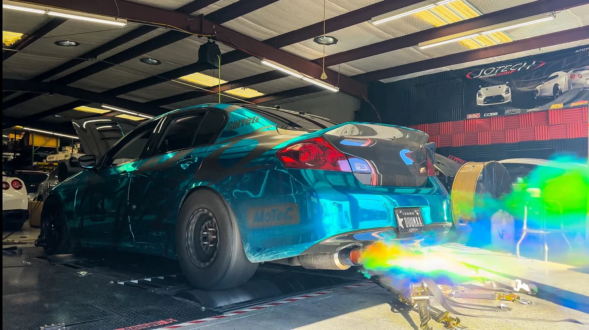 Teal wrapped Infiniti G37 sedan on a dynamometer with exhaust flames during a performance test at Jotech Motorsports.