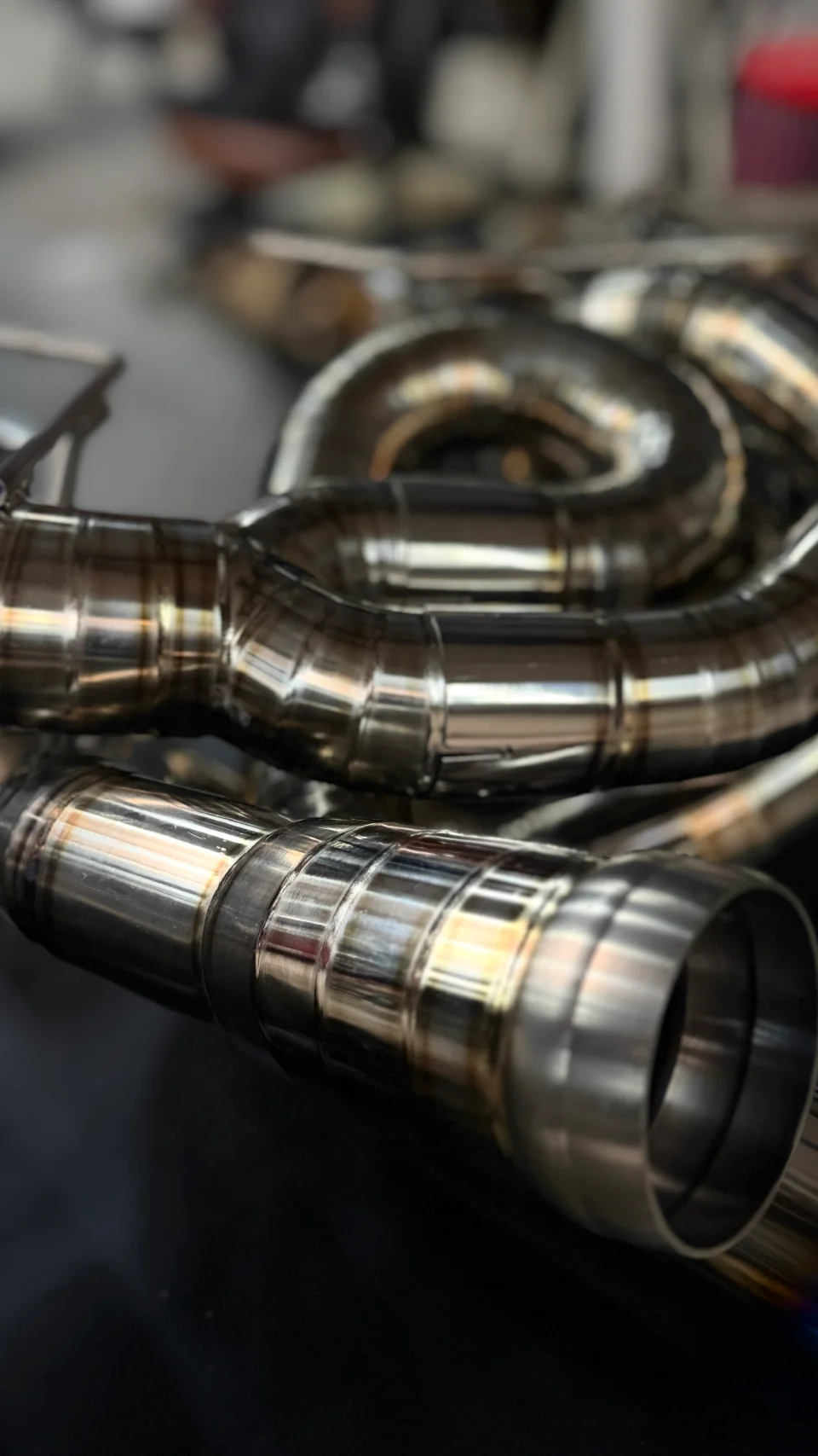 Close-up detail of polished titanium exhaust piping with visible welds, showcasing high-quality fabrication.