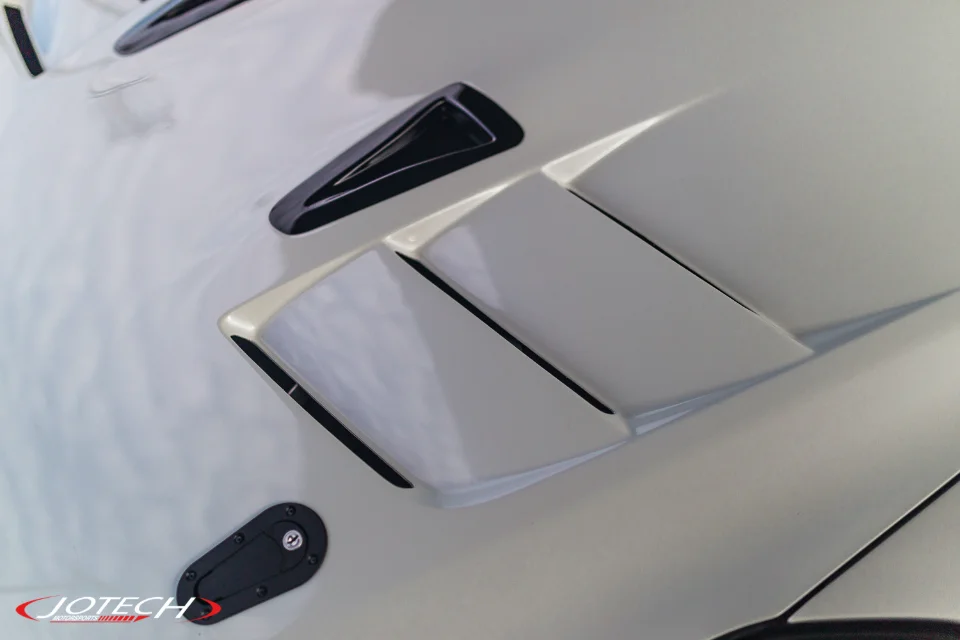 Close-up of a white car's hood featuring black hood vents and a hood pin.