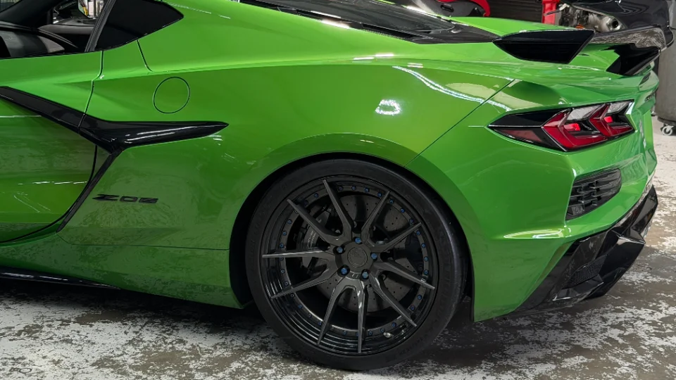 Rear quarter view of a vibrant green Corvette Z06 with custom dark multi-spoke wheels and a rear spoiler.