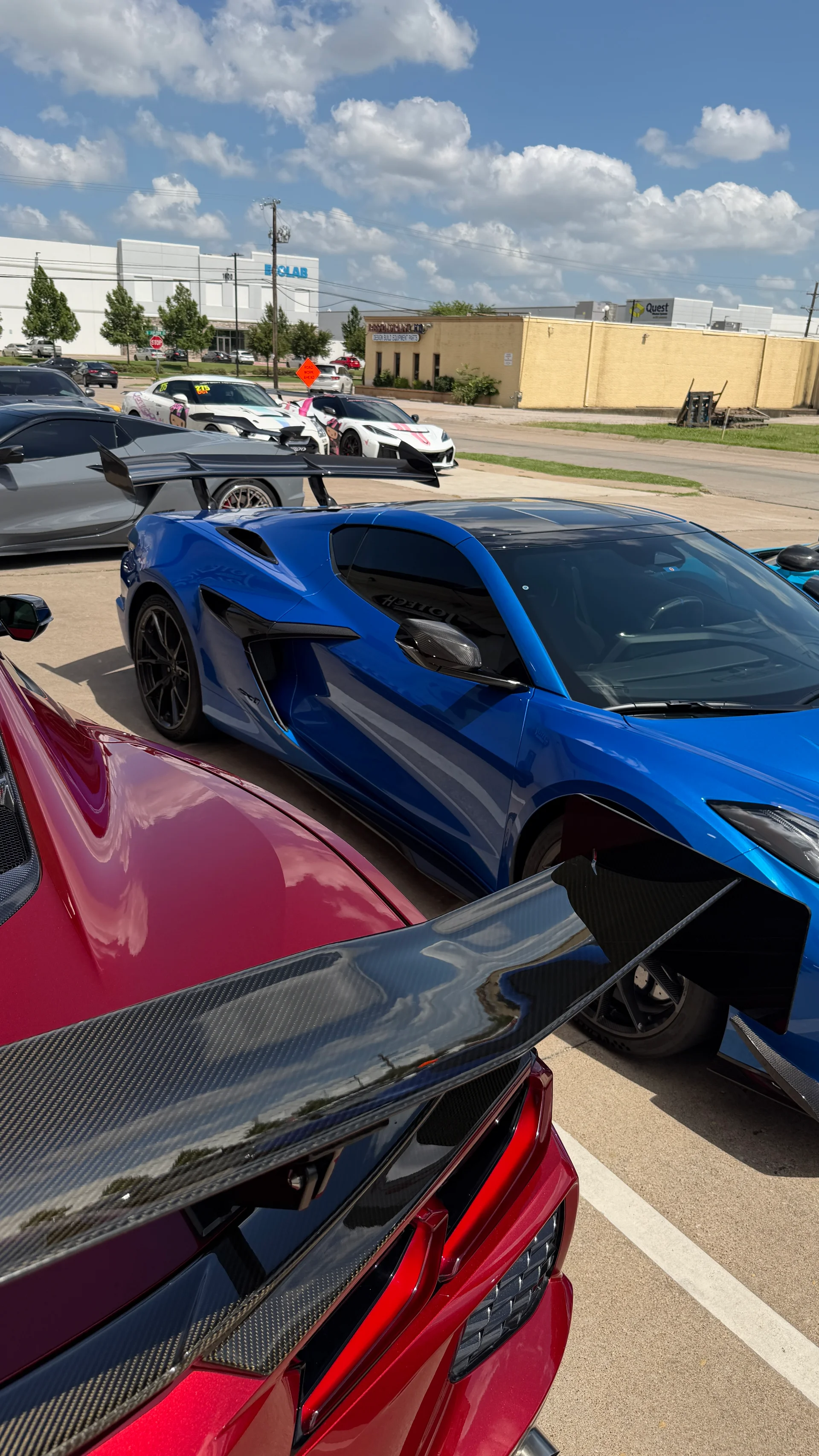 A blue Chevrolet Corvette C8 and a red Chevrolet Corvette C8 with a large carbon fiber rear wing parked outdoors at a car meet.