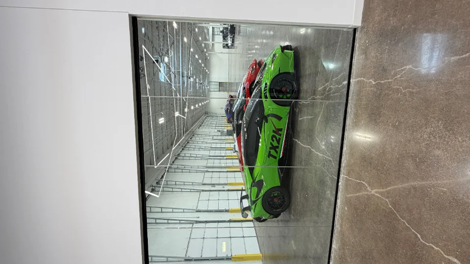 A line of high-performance Lamborghini supercars, including a green TX2K car, parked inside a large, well-lit facility.