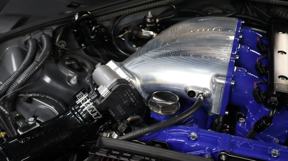 A close-up of a custom engine bay featuring a billet intake manifold and blue fuel rails.